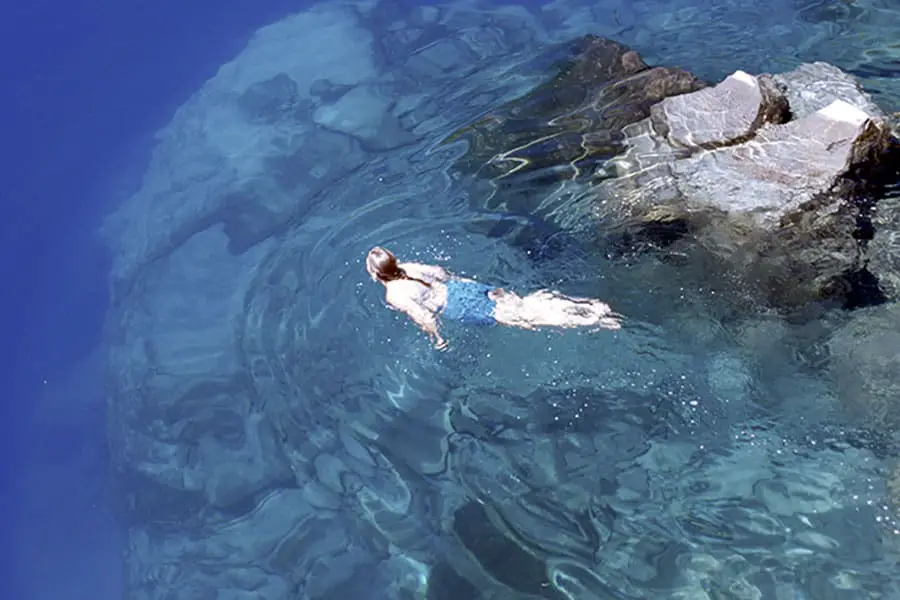 Girl swimming in crystal clear water on rocky shore