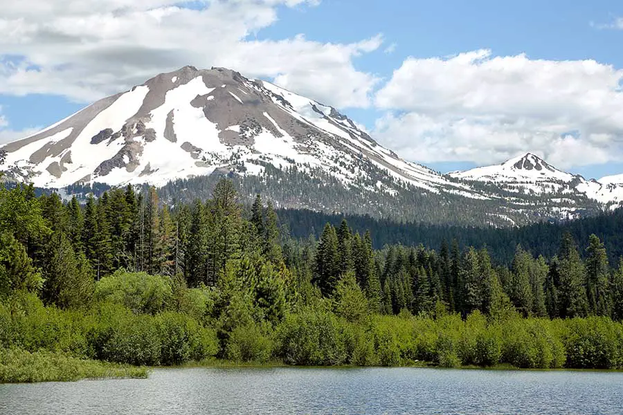 Snow capped Mount Lassen and beautiful Manzanita lake surrounded by evergreen trees
