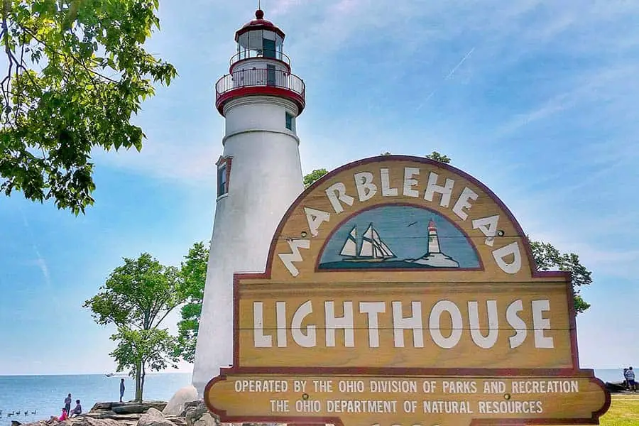 Lighthouse sign in front of white lighthouse near the seashore