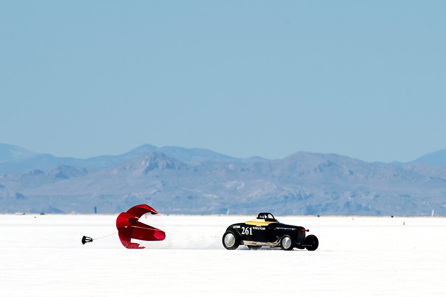 Black race car opens red parachute on salt flats