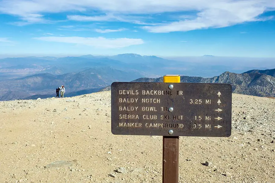 Hikers at mountain summit nearing wooden trail sign