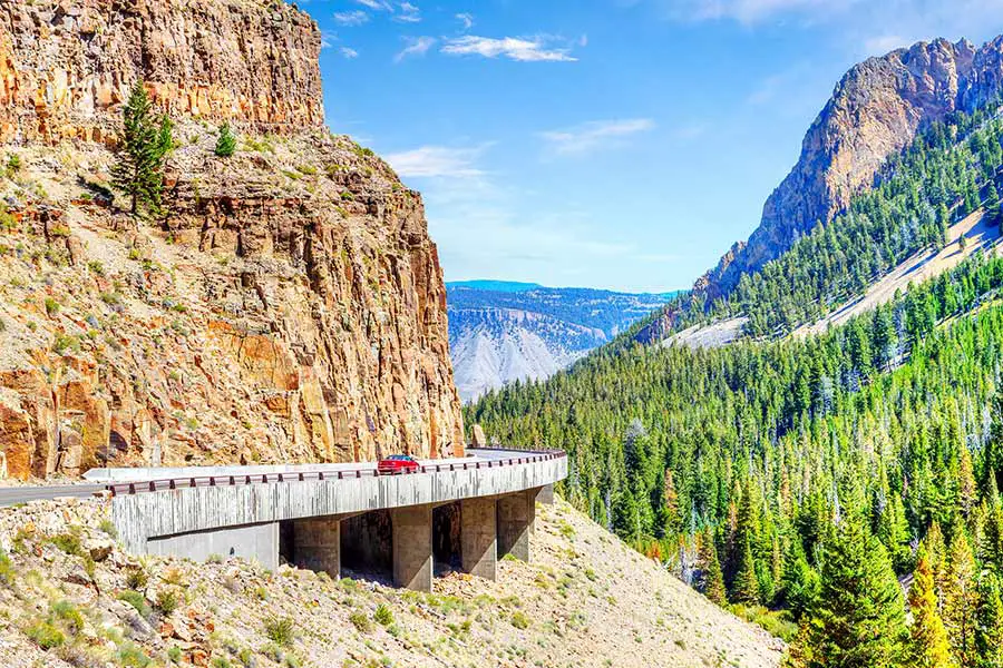 Red car on viaduct bridge traversing a steep rocky canyon valley