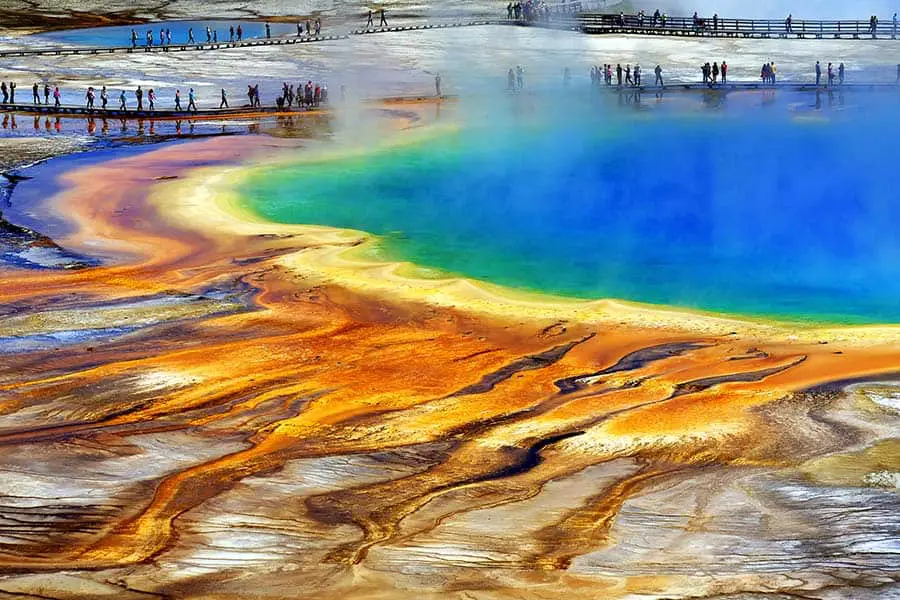 Multi colored water in large hot spring, tourists walking on boardwalk