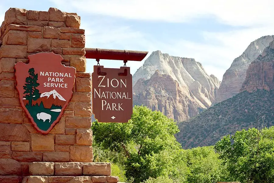 Zion National Park entrance sign with steep canyon walls in background
