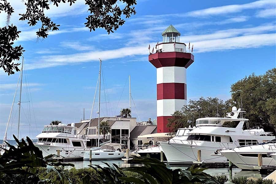 Pleasure boats docked at pier next to red and white lighthouse