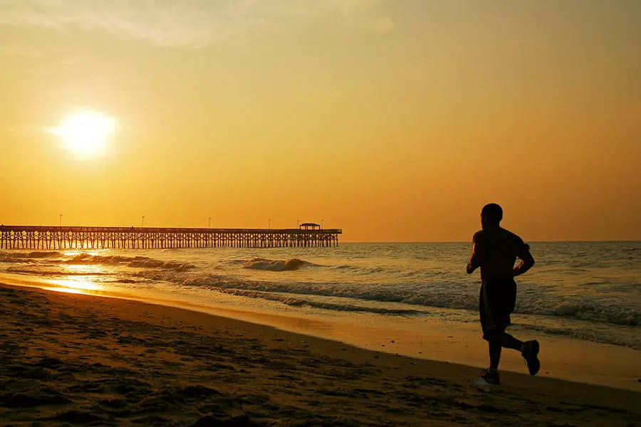 Silhouette of jogger on beach at sunrise, long pier juts out into ocean