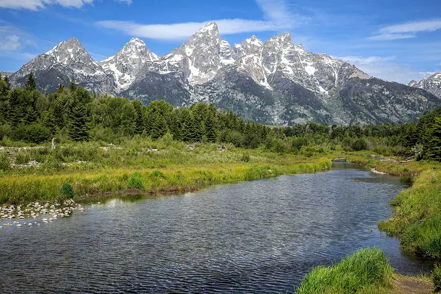 River flows through a lush valley with Grand Teton mountain range in background