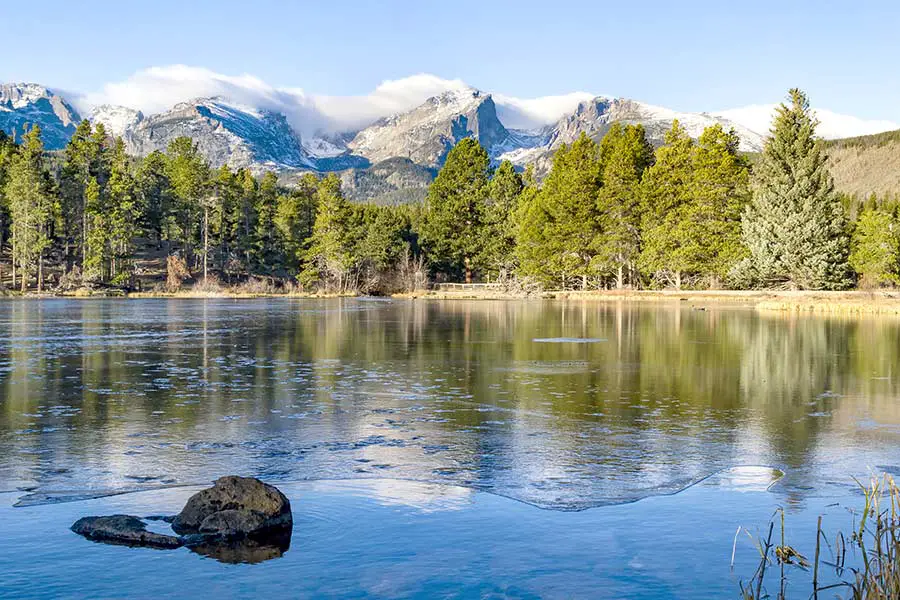 Scenic Sprague Lake begins to form ice as colder weather sets in, majestic mountains in background